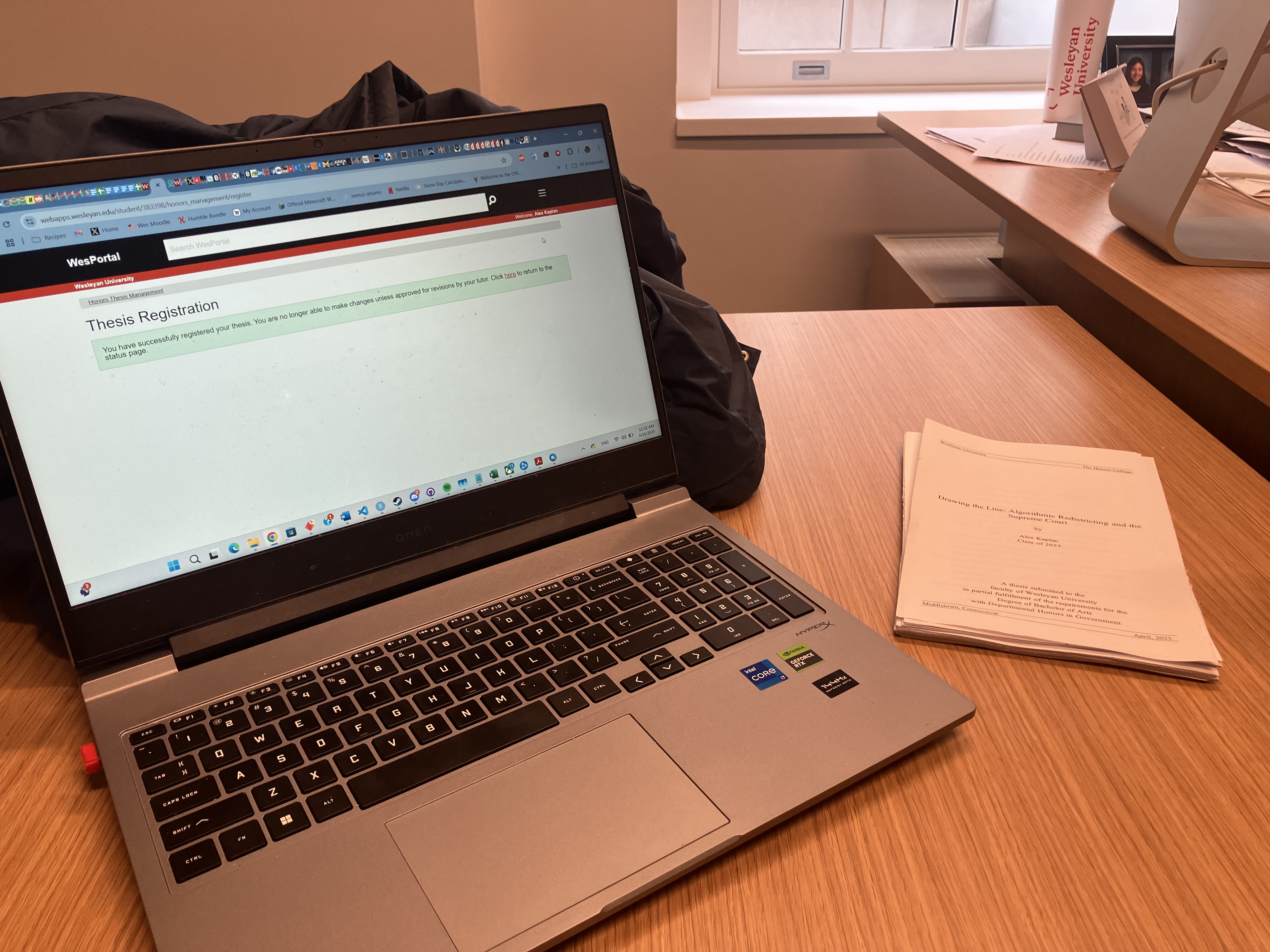 An image of the submission page for the thesis on a laptop. Next to the laptop, on the table, sits a print test of the thesis.